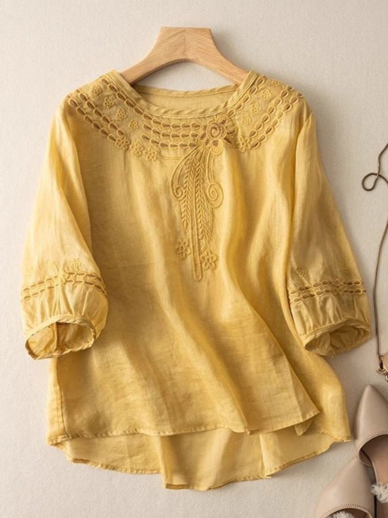 Yellow blouse with lace details on a hanger against a light background