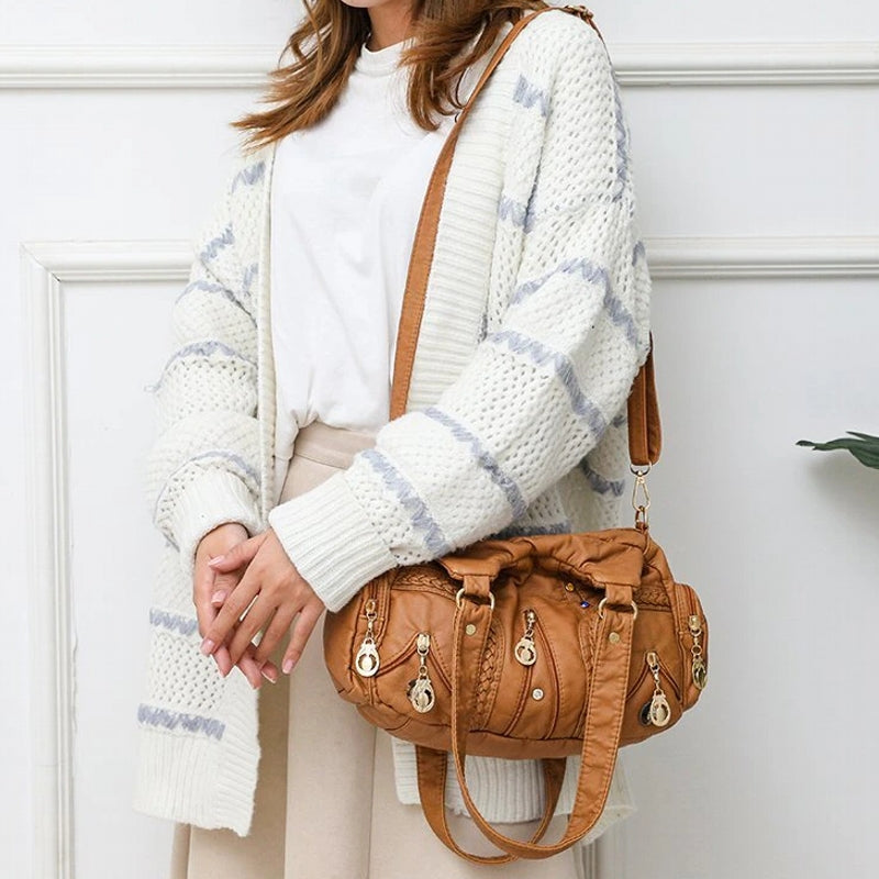 Person wearing a white sweater with blue stripes and holding a brown handbag against a white wall.